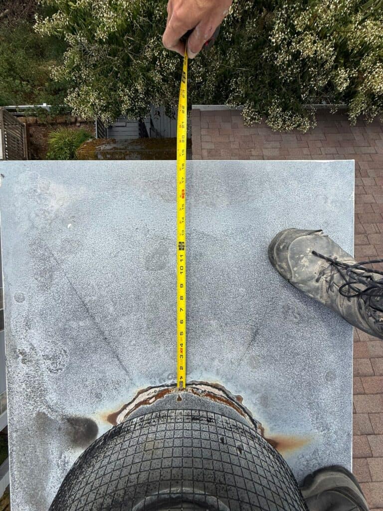 Technician measuring the top of a chimney crown with a tape measure before installing a new cap.