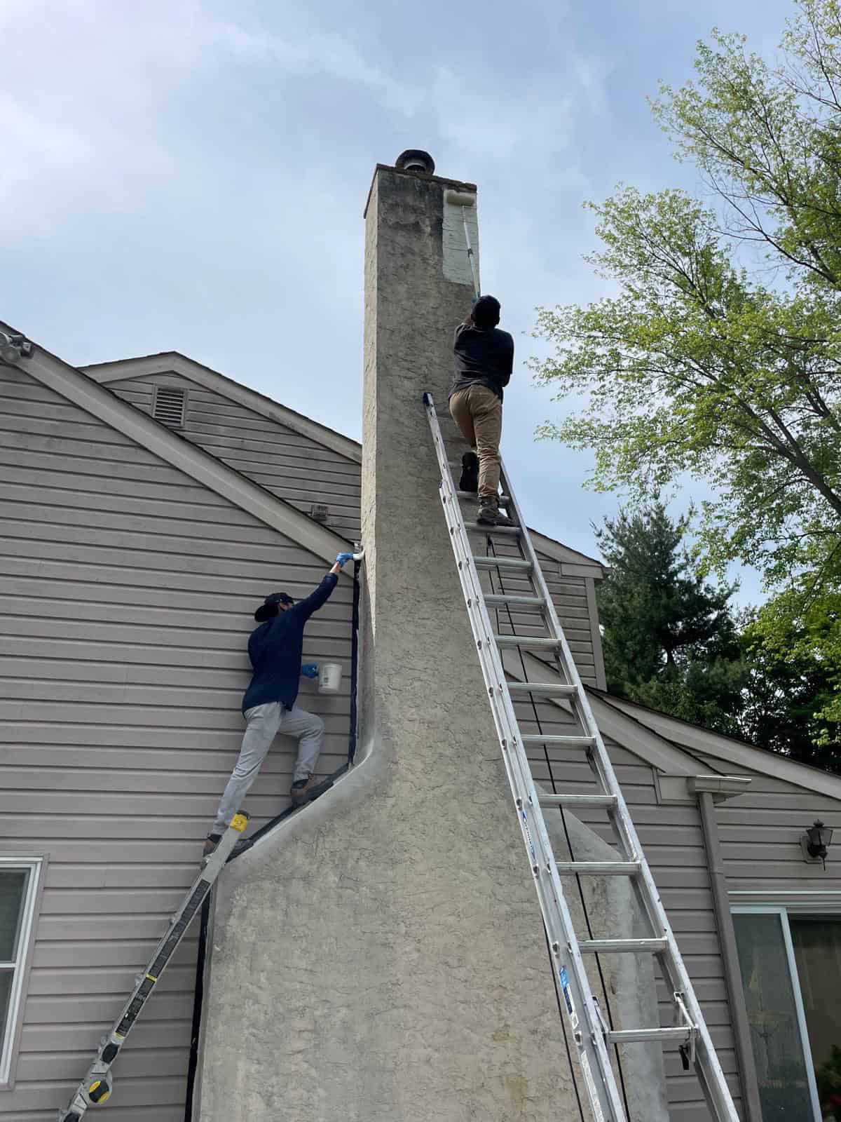 Technicians repairing a tall stucco chimney using ladders.