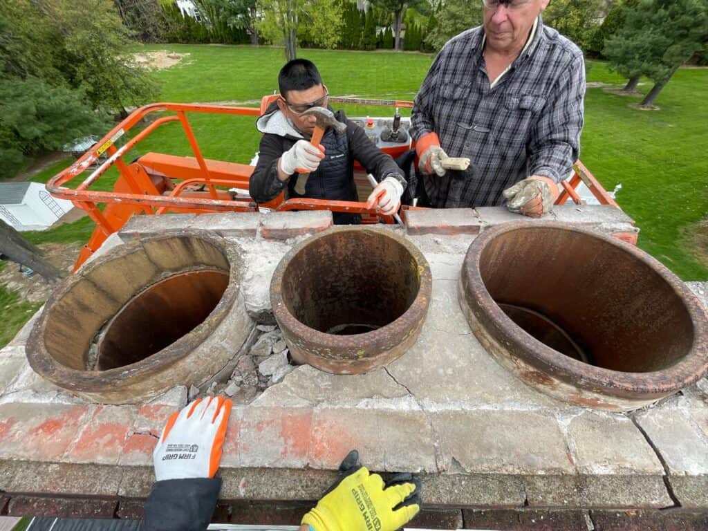 Technicians inspecting a large chimney with three exposed round flue openings.