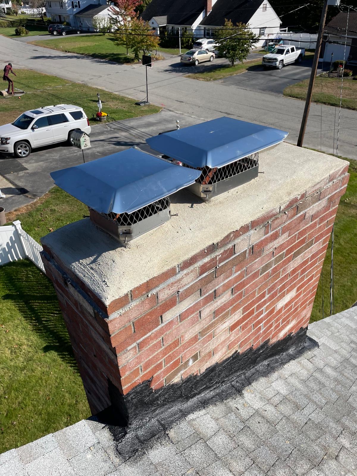 Two stainless chimney caps installed on a wide masonry chimney.